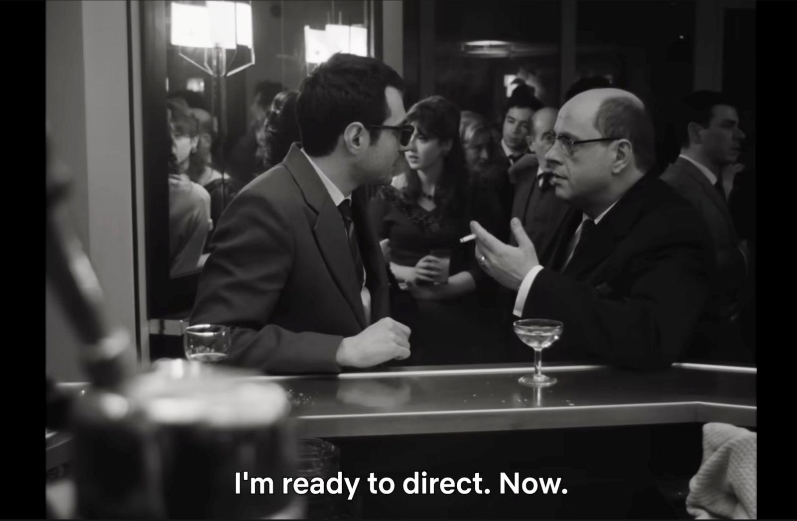 A black-and-white photo is captioned with the line &ldquo;I&rsquo;m ready to direct. Now.&rdquo; Two men are speaking to each other in a crowded bar.