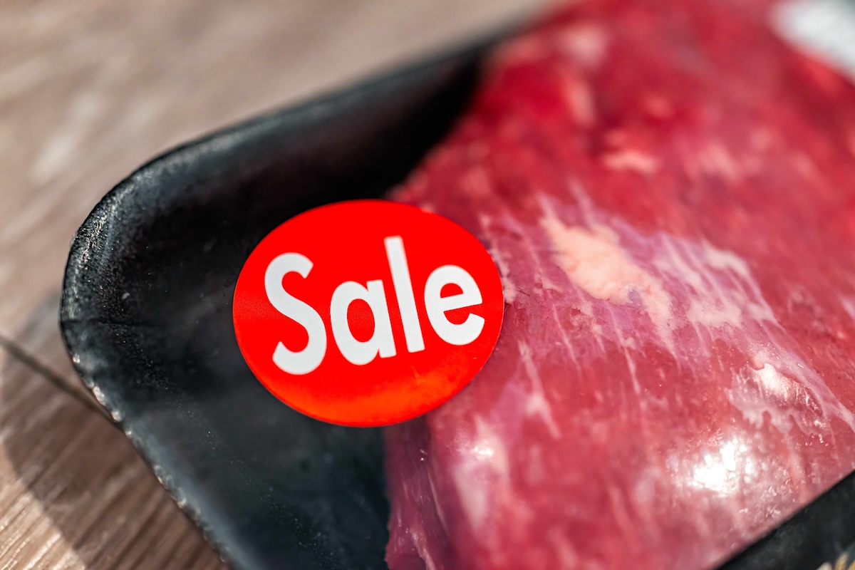 A close-up photo of a grocery store steak in plastic wrap on a black Styrofoam tray features a red &lsquo;Sale&rsquo; sticker on the package.