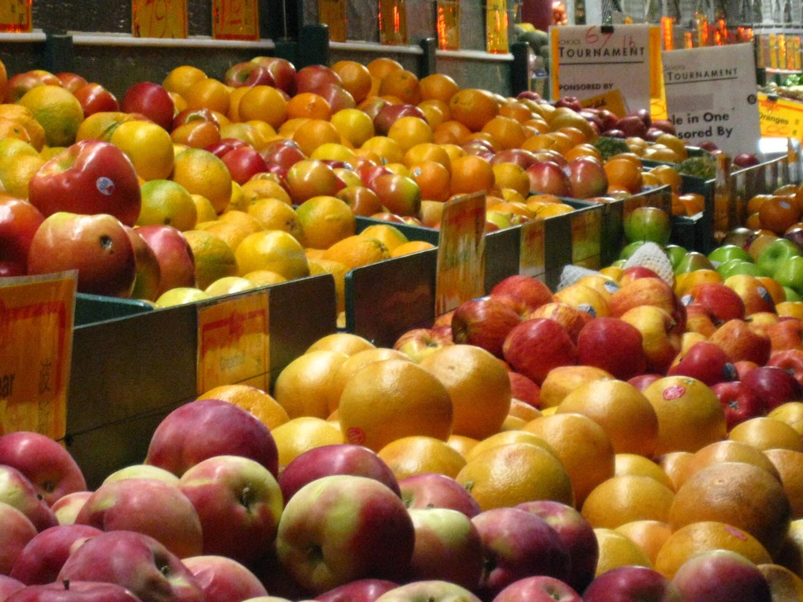 Piles of apples and oranges in containers part of a grocery-store fruit stand. 