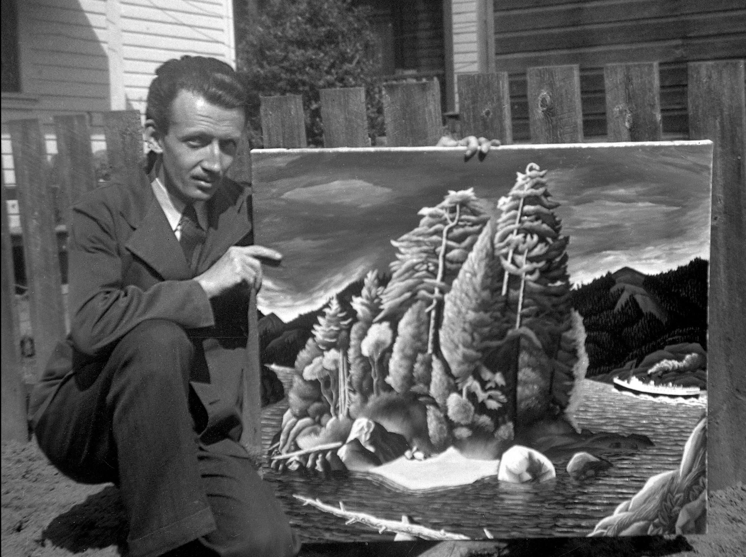A black-and-white photo of E.J. Hughes depicts a man with dark wavy hair and a moustache crouching next to a large landscape painting of trees on an island. He is in a yard with a wooden fence in the background.