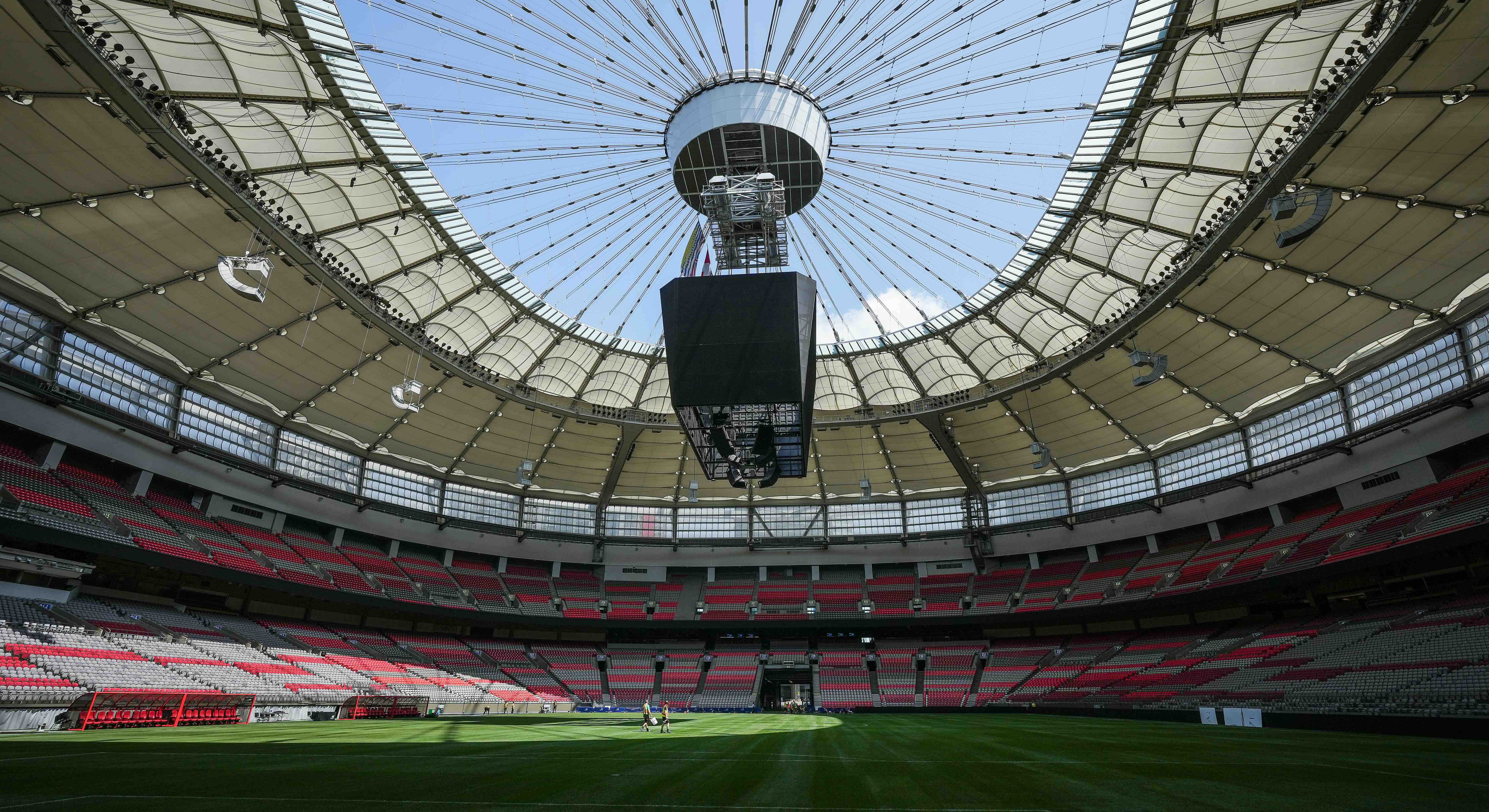 An interior view of BC Place stadium shows a green soccer field, stadium seating and an open roof to a blue sky.