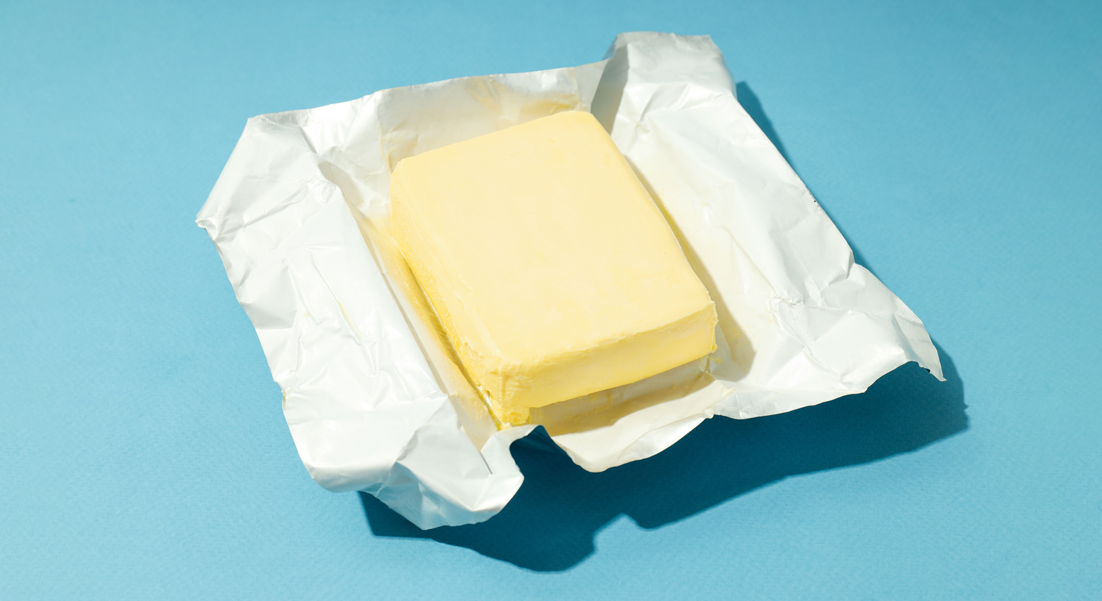 A package of butter lays open under bright light on a blue background.