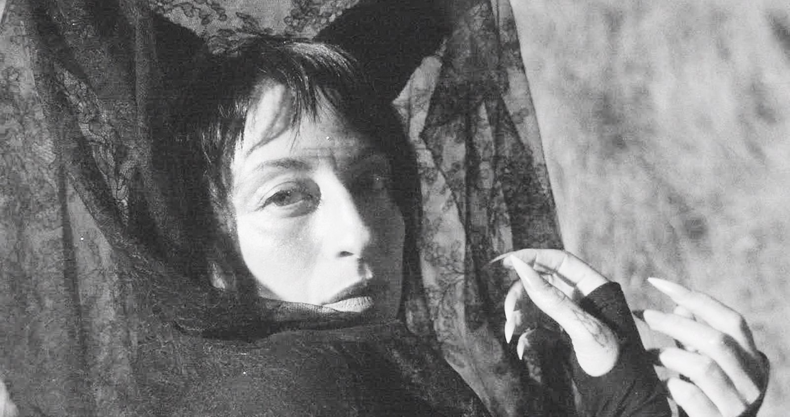 A black-and-white abstract photograph of Ora Cogan depicts the artist in bright light in a swirl of dark lace fabrics.