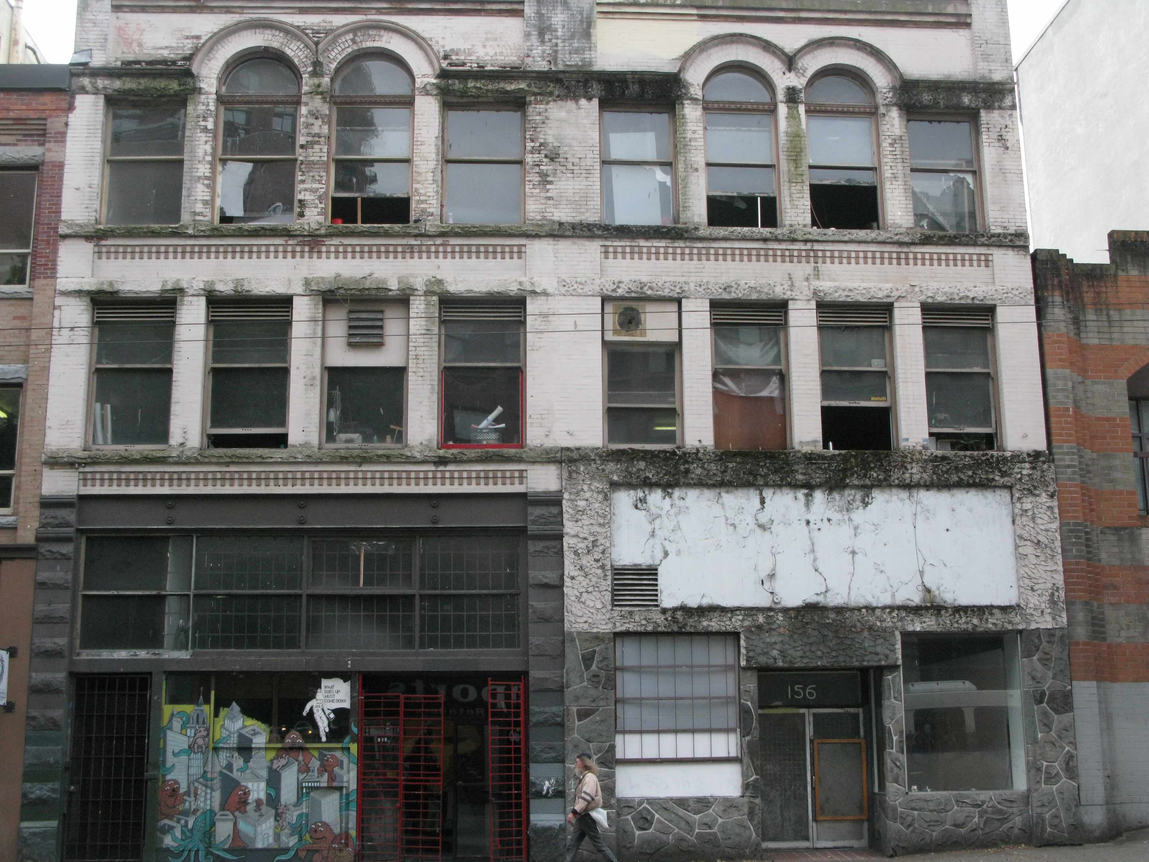 The fa&ccedil;ade of an older light grey three-storey building features a distinctive set of red gates on the ground floor, which was the original home of Red Gate Arts Society.
