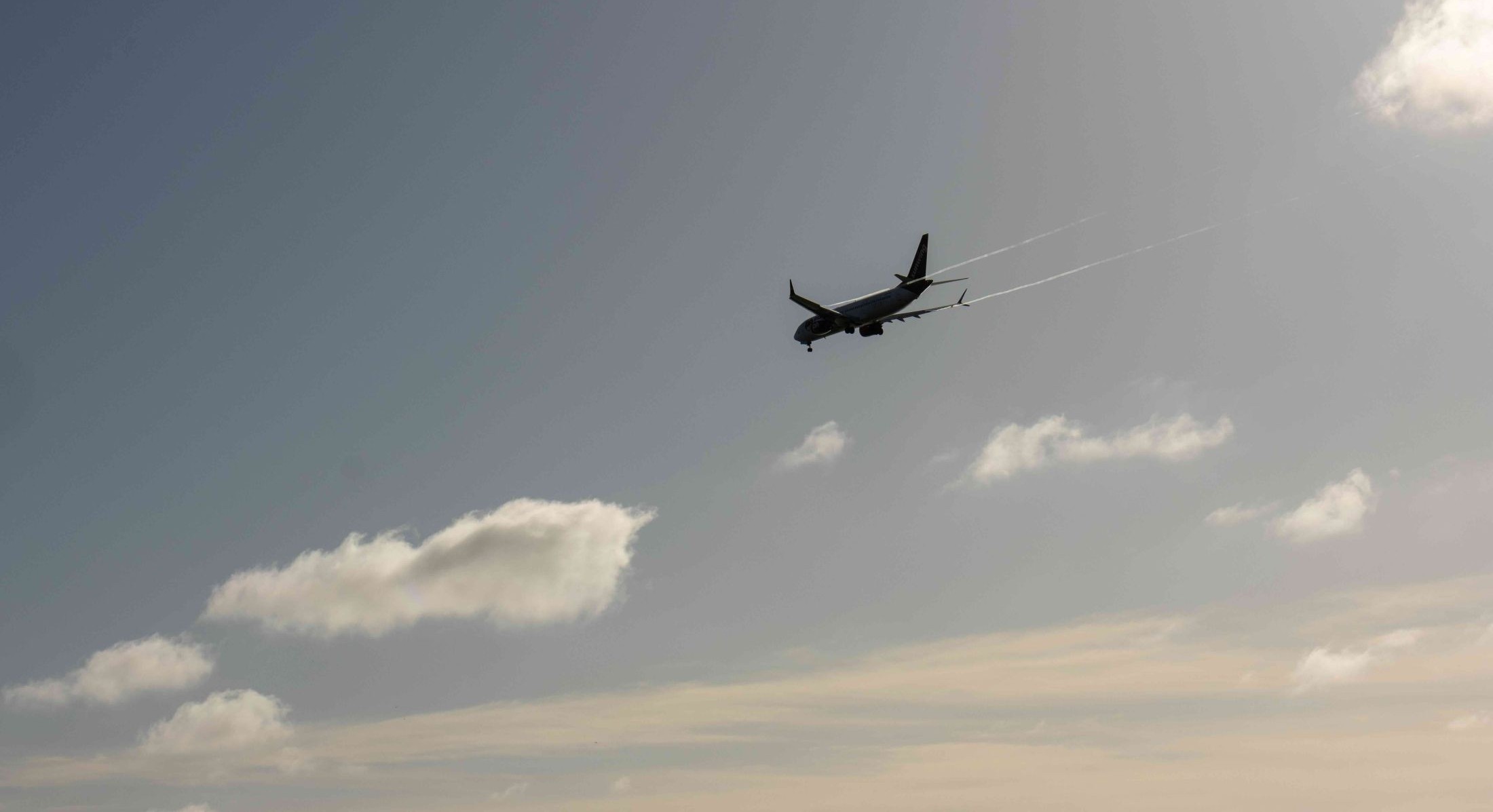 A passenger jet in silhouette against a blue sky with clouds. 