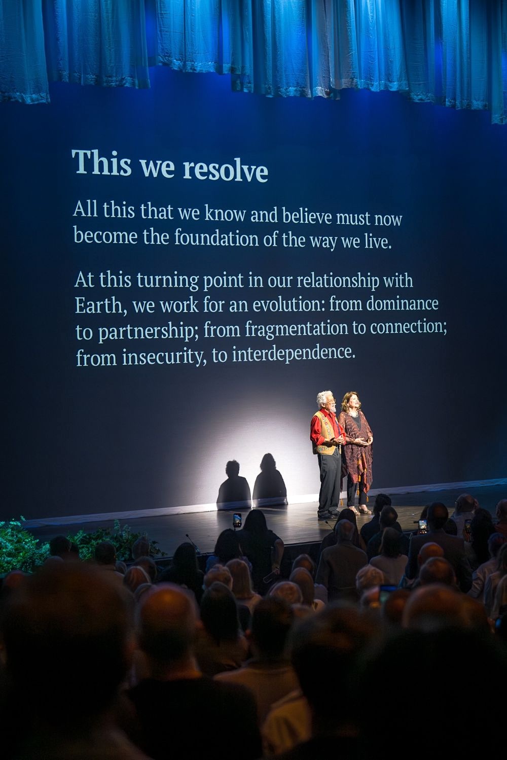 David Suzuki and Tara Cullis are spotlighted onstage with a screen behind them projecting the words from the Declaration of Interdependence.
