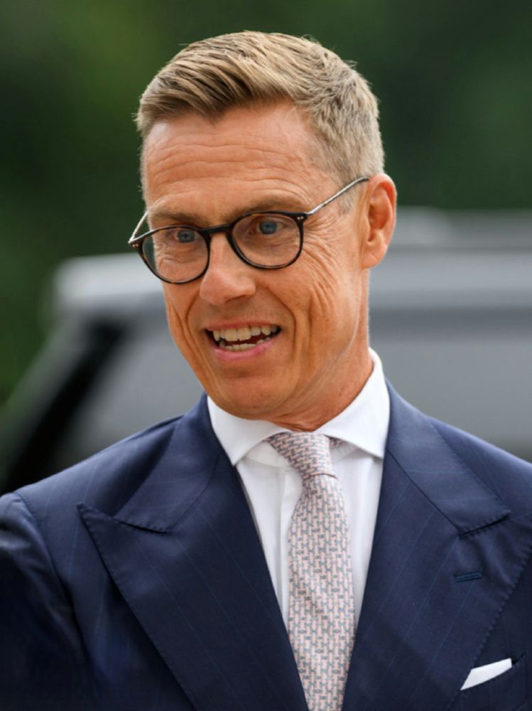 Alexander Stubb has short blond hair and glasses. He is wearing a navy suit over a white shirt and patterned light pink tie.