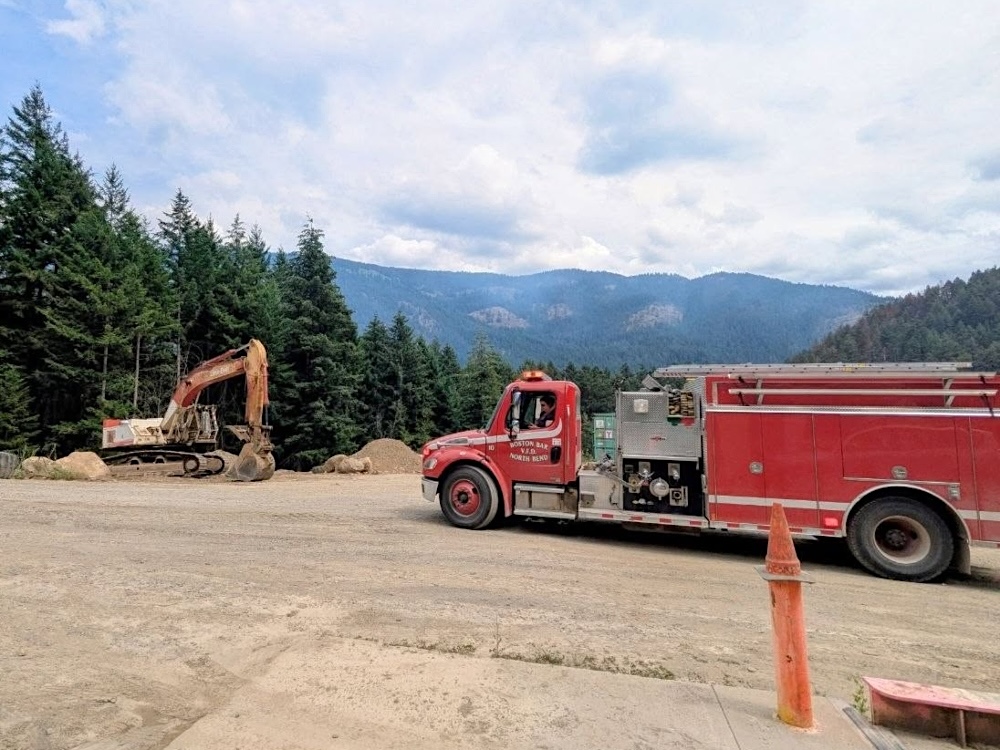 A fire engine sits on a gravel road beside a backhoe.