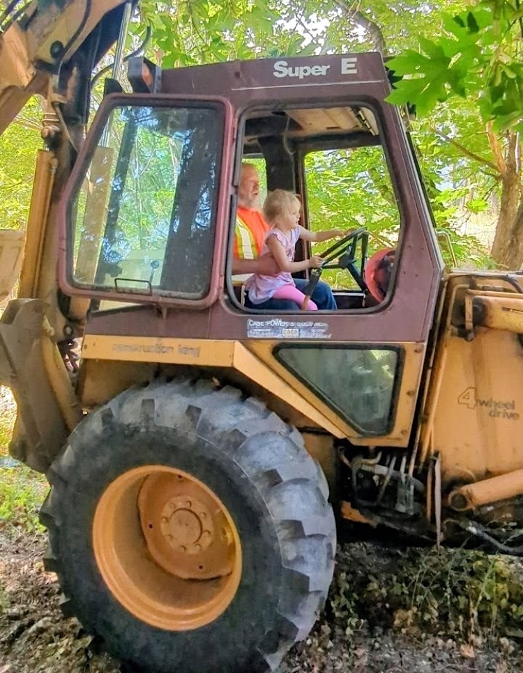 A young girl sits on the lap of an adult in a piece of heavy machinery. 