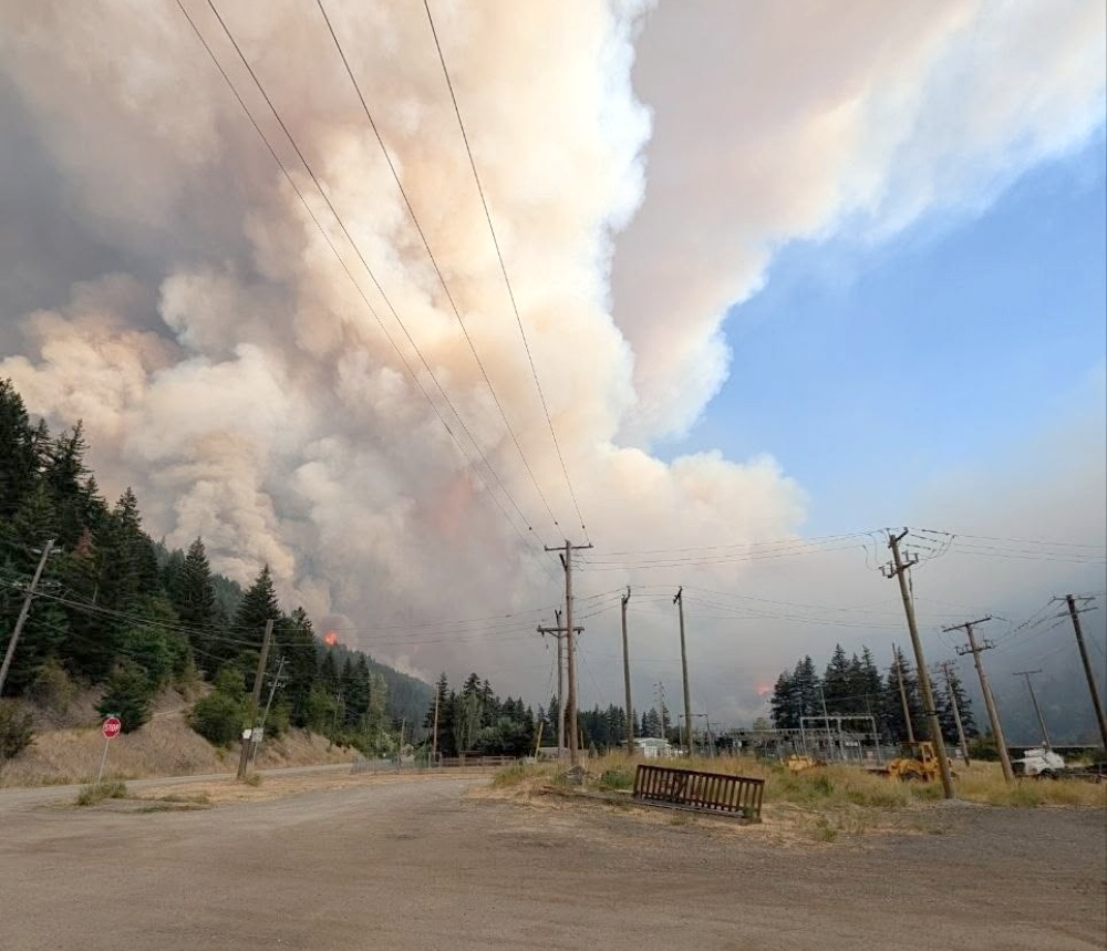 A massive plume of smoke covers much of the sky. Some flames are visible.