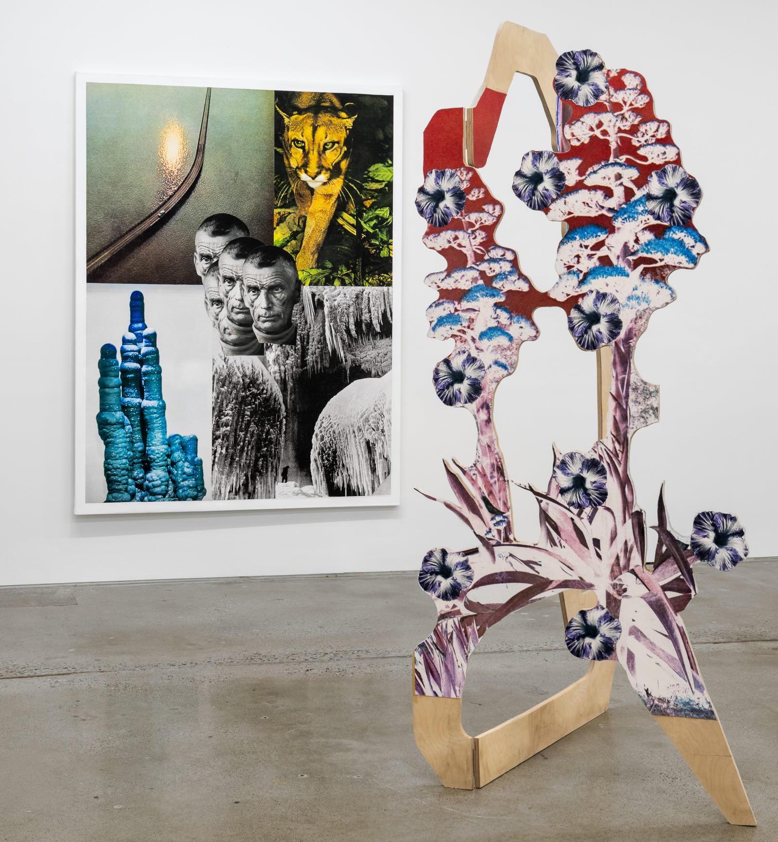 A tall wooden sculpture inlaid with abstract colour photographs of plants and flora stands in front of a large multimedia piece of artwork hung on a white wall.