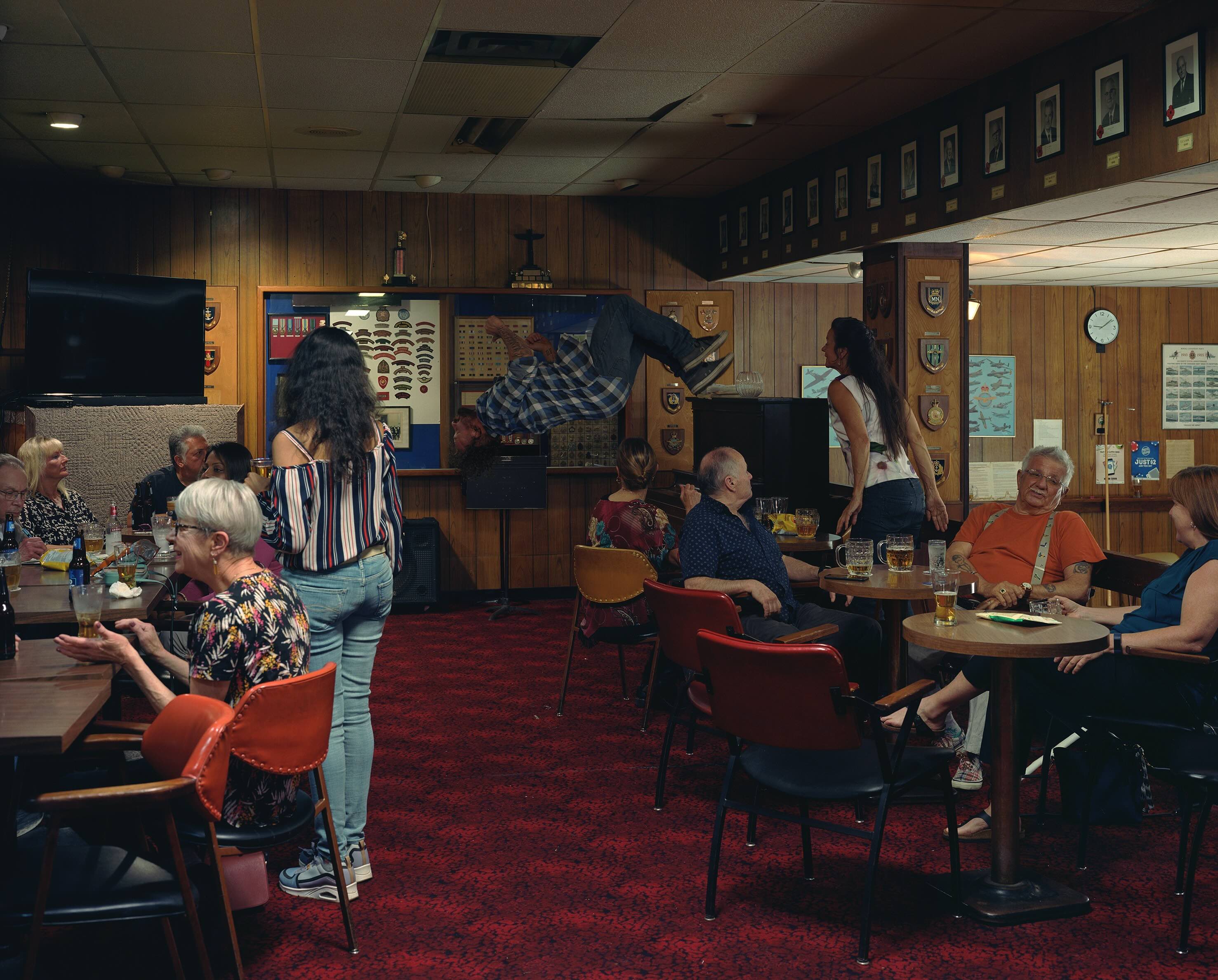 Jeff Wall&rsquo;s 'In the Legion' is a conceptual photograph that depicts the dimly lit interior of a legion hall where people are drinking beer and socializing. In the background a man is doing a backflip.