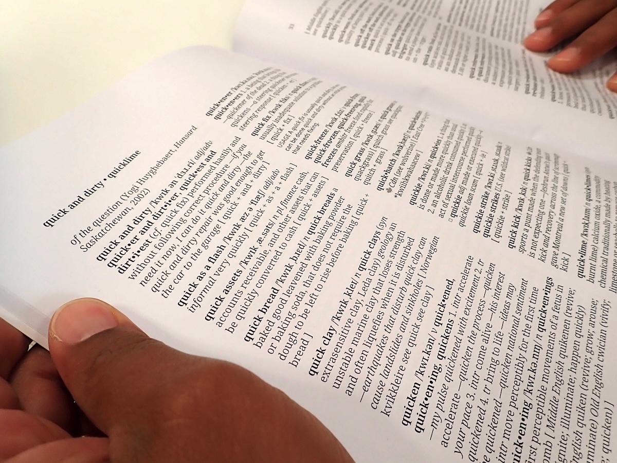Two hands hold open a dictionary section for the letter Q. The page on the left features a section head that reads &lsquo;quick and dirty; quicklime.&rsquo;