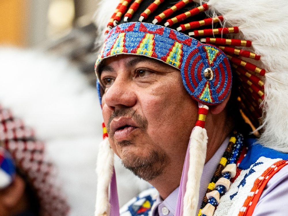 An Indigenous man with a headdress speaks.