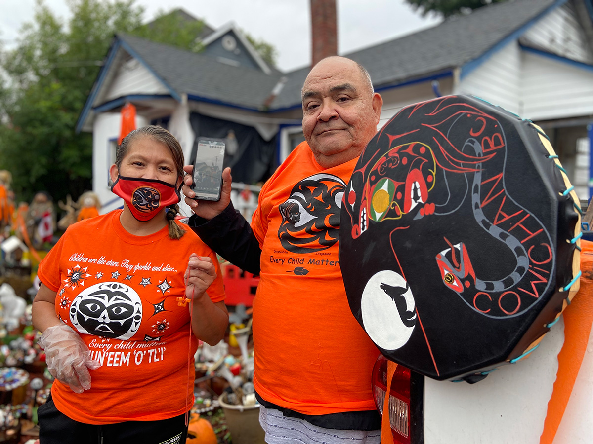 Mary Joseph and Tim Joseph stand in front of their orange-decorated home as marchers walk by.