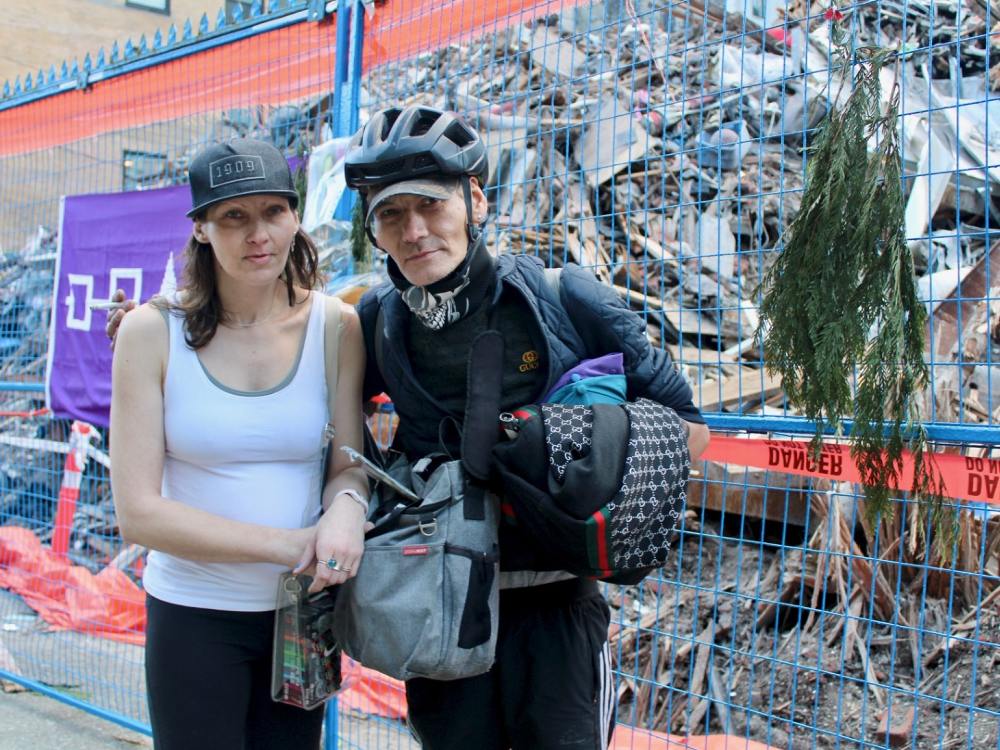 A woman and a man stand in front of a pile of rubble from a building that was torn down after a fire.