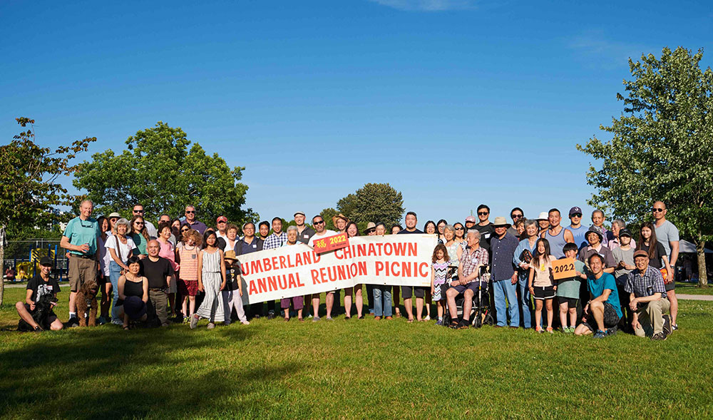 A group photo of the Cumberland Chinatown reunion picnic group on June 26, 2022. They are holding a banner that reads &ldquo;Cumberland Chinatown Annual Reunion Picnic.&rdquo;