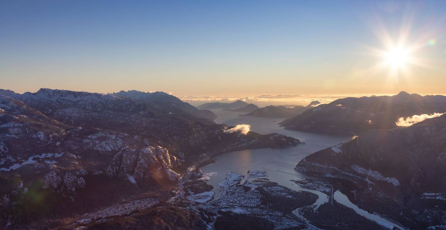 An aerial view of the Howe Sound; there is snow on the ground, and Squamish is visible skirting the water.