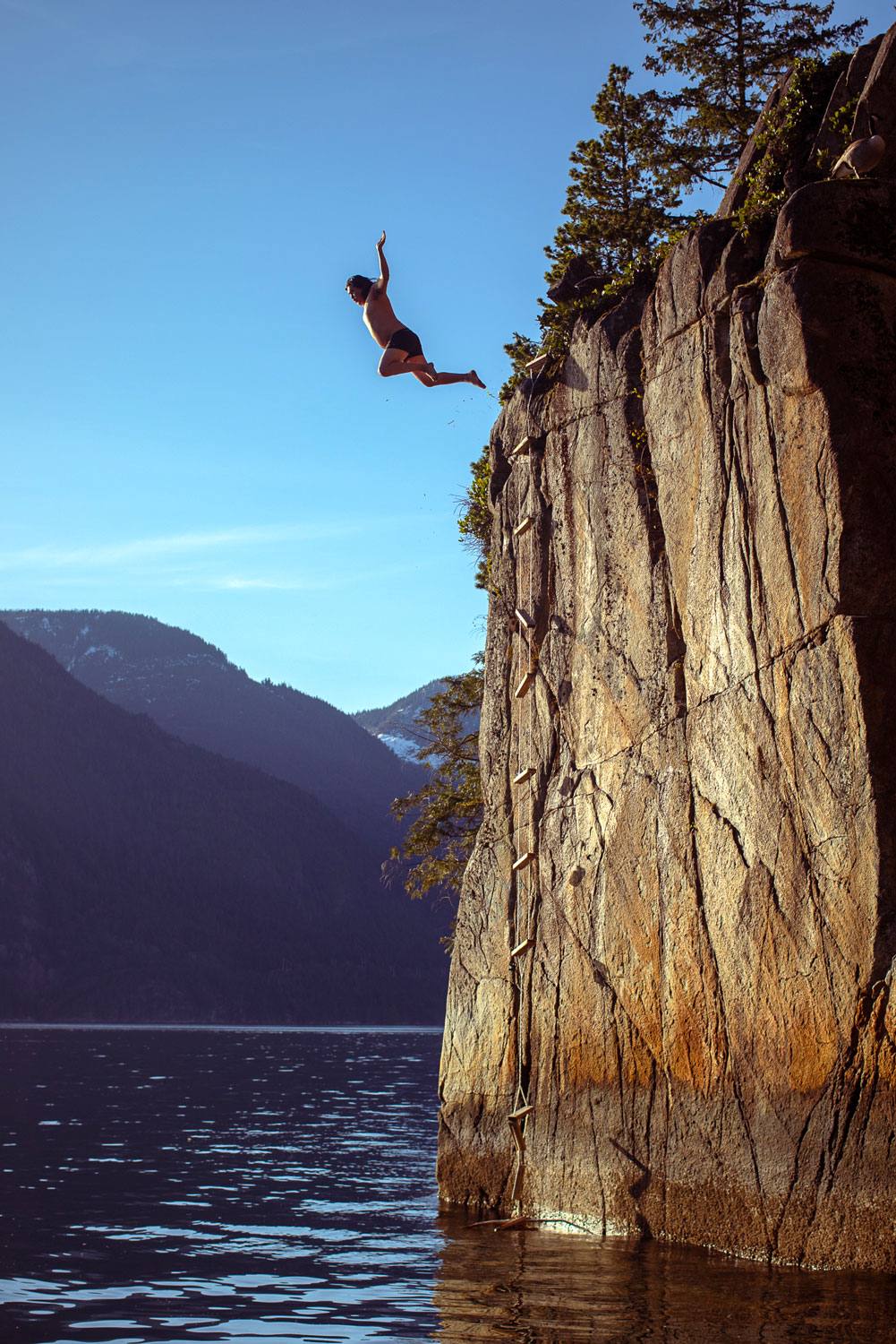 A man jumps from a cliff that&rsquo;s about seven or eight metres high, into the ocean below.