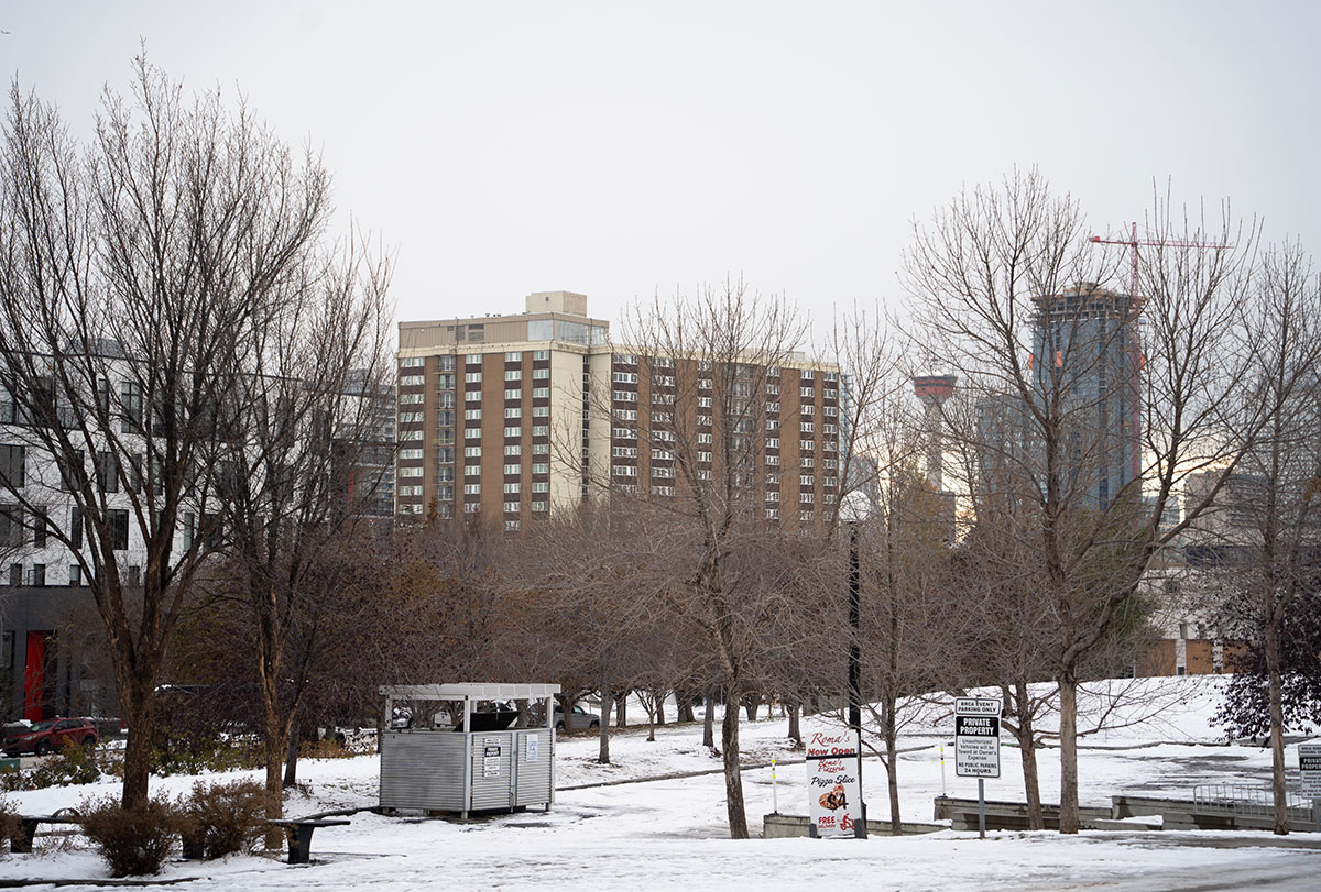 Bridgeland Place apartment building on the horizon of a white sky in winter. Leafless trees cover the foreground landscape.