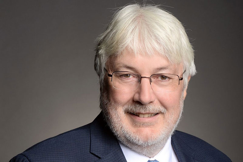 Glen Jones, a smiling middle aged, white haired white man in a blue suit jacket.