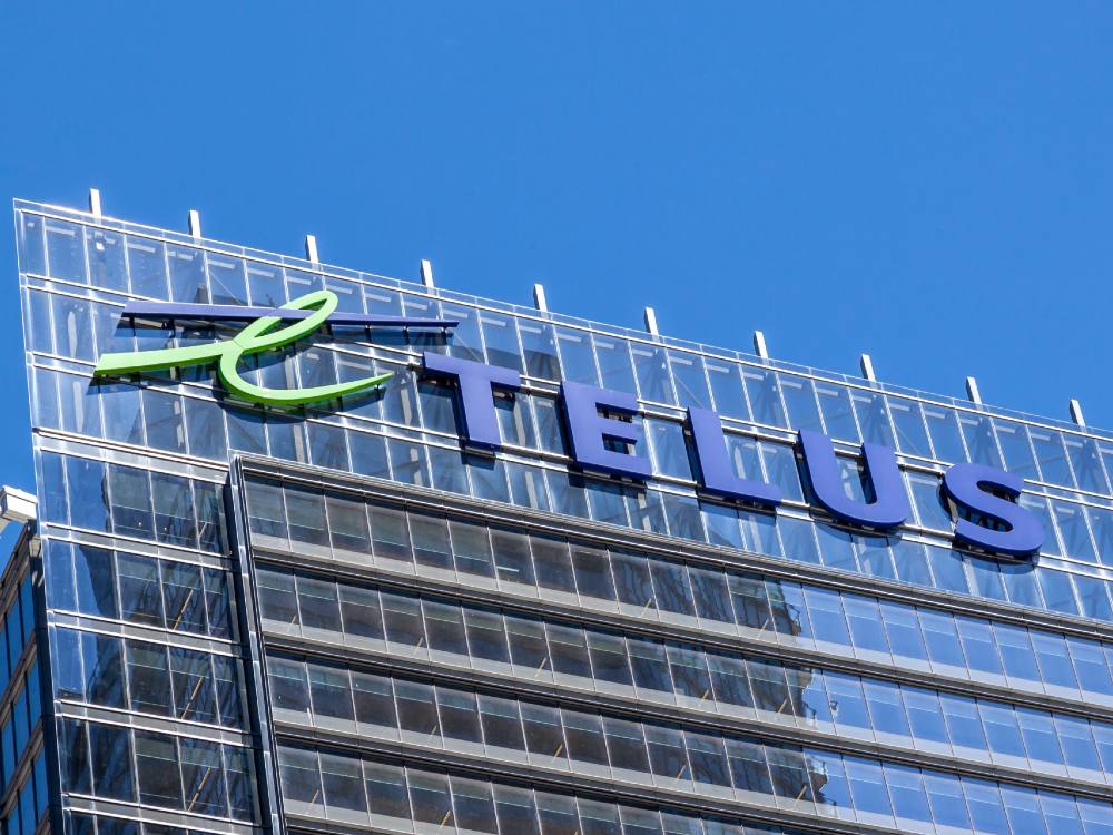 The top seven floors of a glass office building under a clear blue sky, with the TELUS logo in large letters on the building.