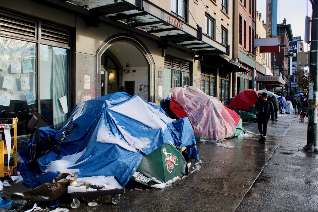 Tents and makeshift shelters stretch along a wet sidewalk in Vancouver&rsquo;s Downtown Eastside.