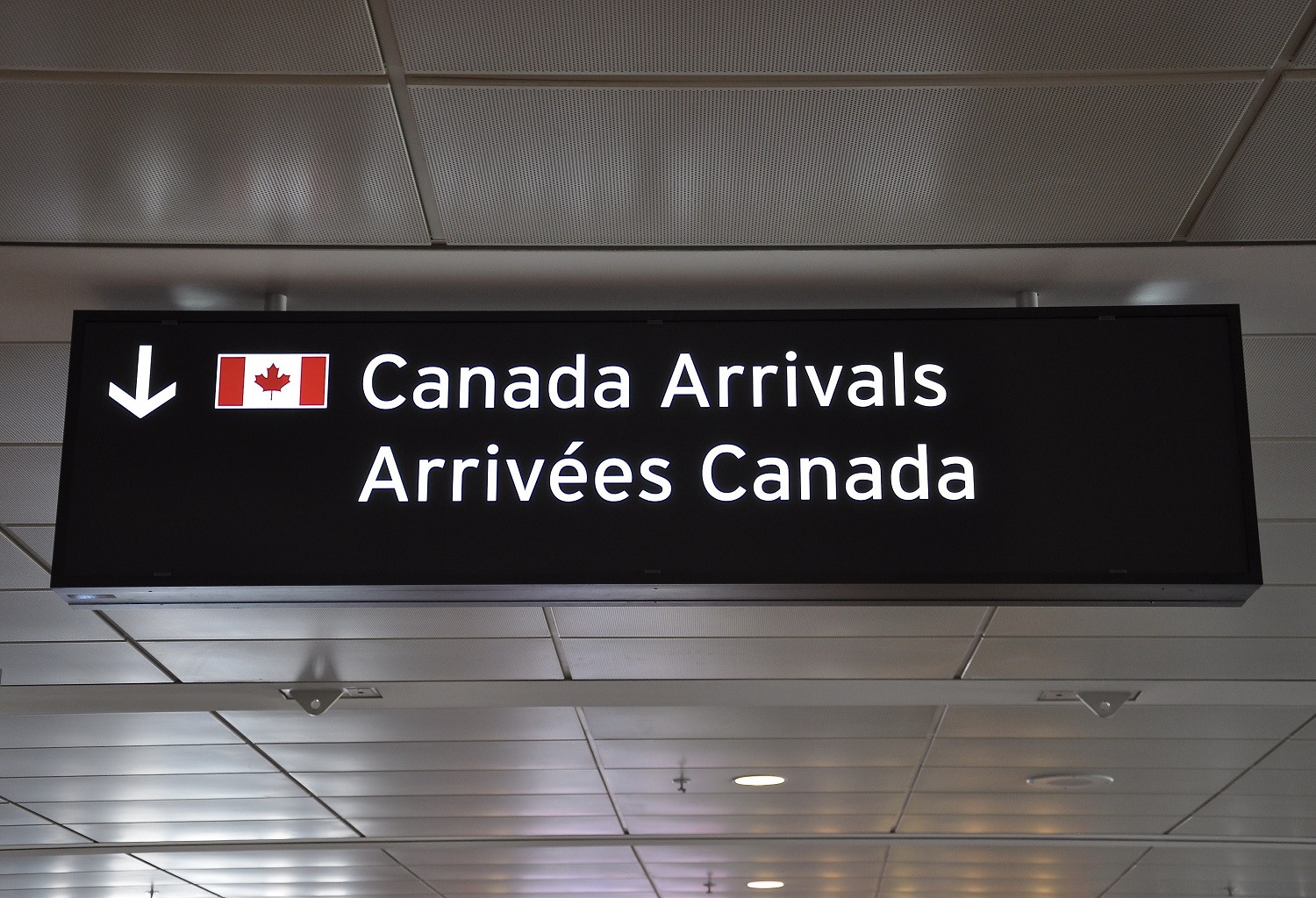 An airport sign reads, “Canada Arrivals / Arrivées Canada.” 