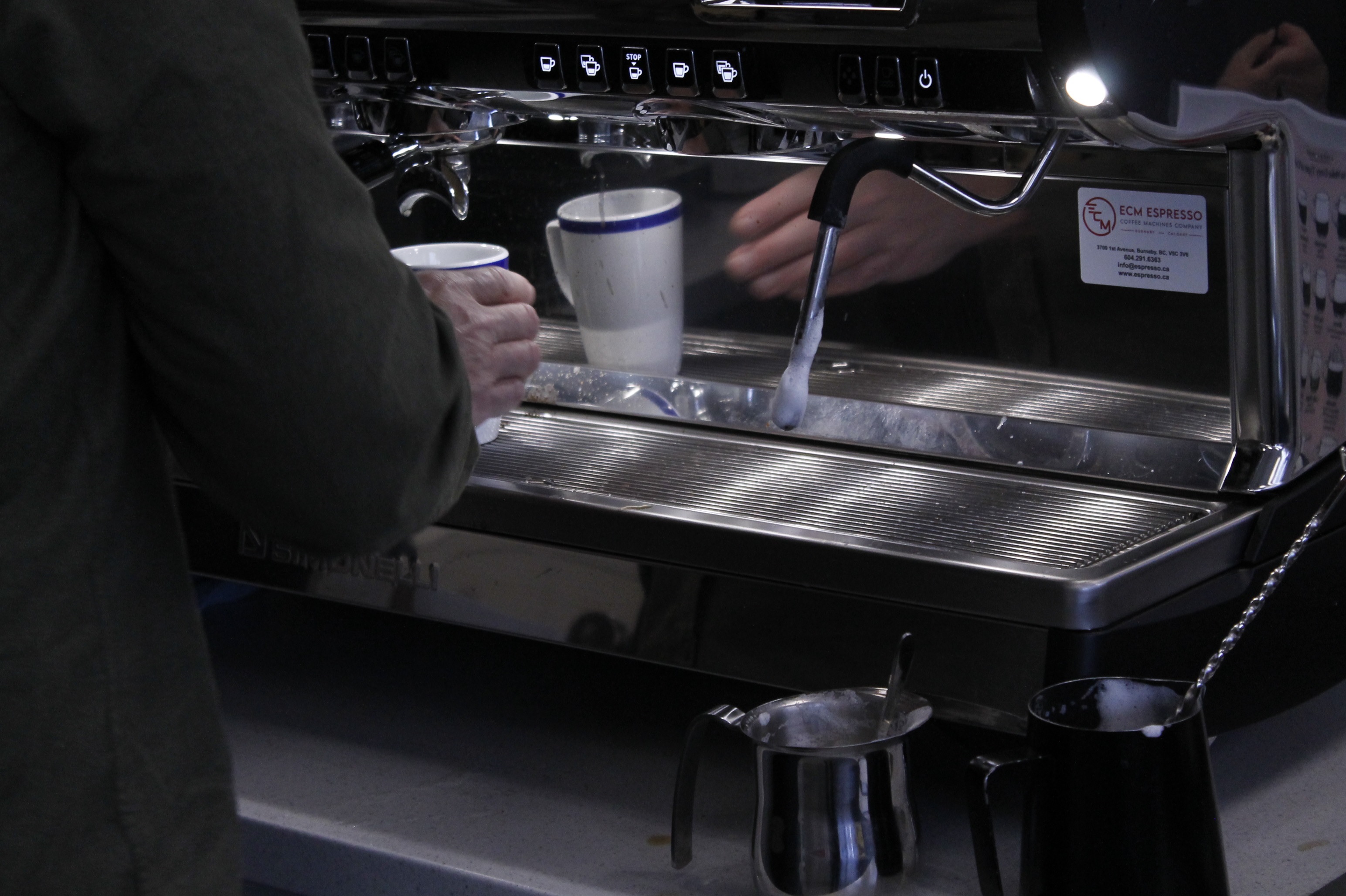 Close-up of an espresso machine, wiith a hand holding a cup to collect the espresso.