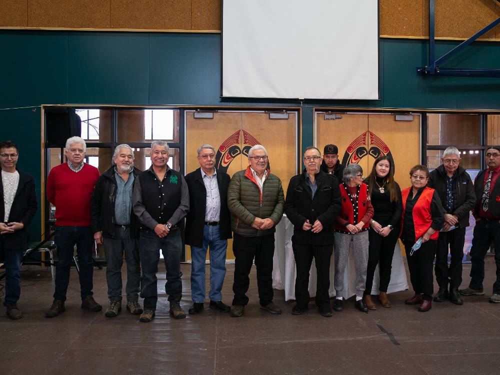 A group of people stand lined up against the wall of a gymnasium. 