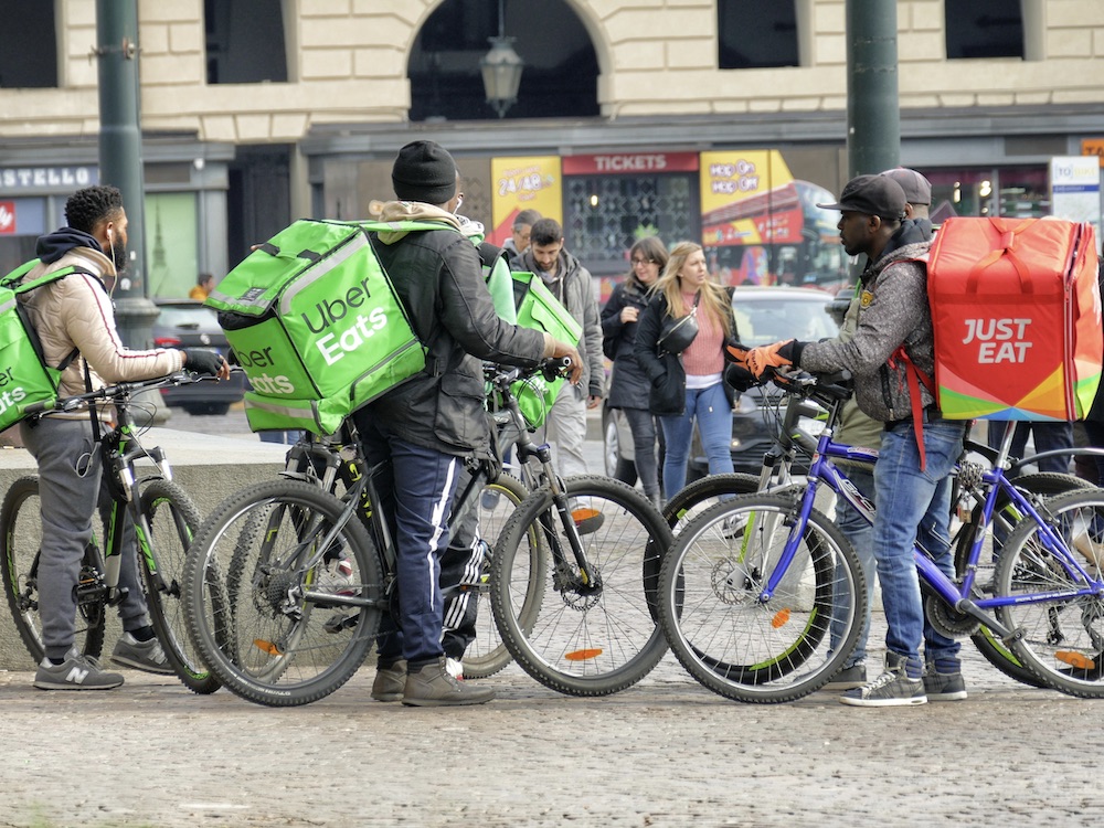 Couriers from Uber Eats and Just Eat gather in a public square.