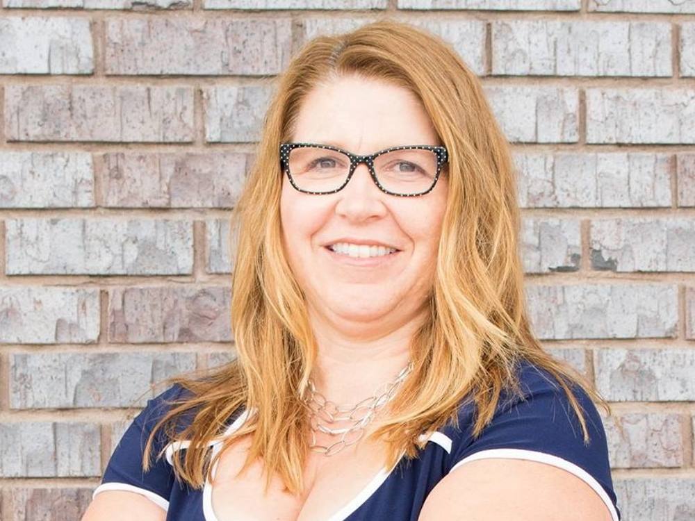 A headshot photo of Tracy Allard, posing in front of a brick wall. 