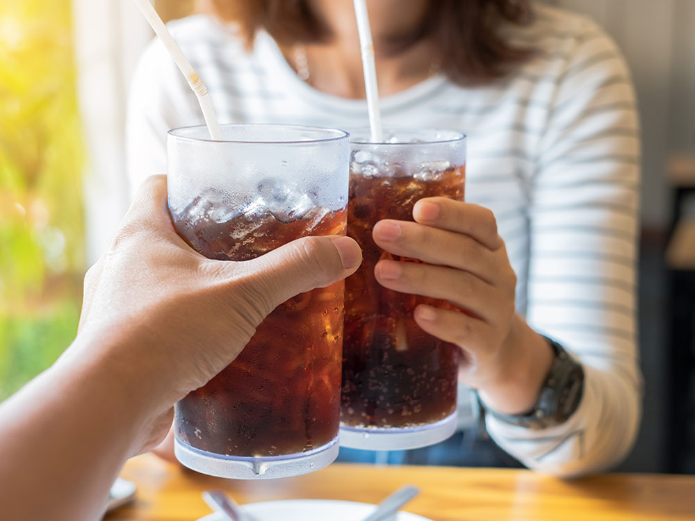 Two people cheers non-alcoholic beverages (sodas) in a social setting, across a table.