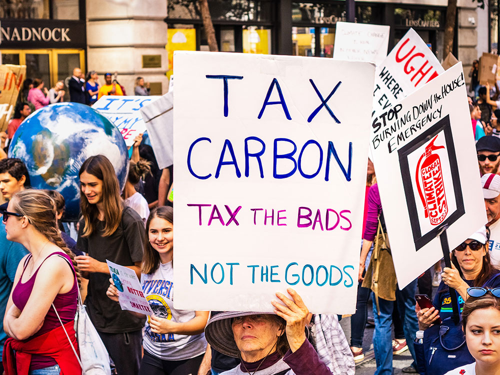 People march in a protest carrying signs that say &ldquo;Tax carbon Tax the bads, not the goods&rdquo; and &ldquo;stop burning down the house.&rdquo;