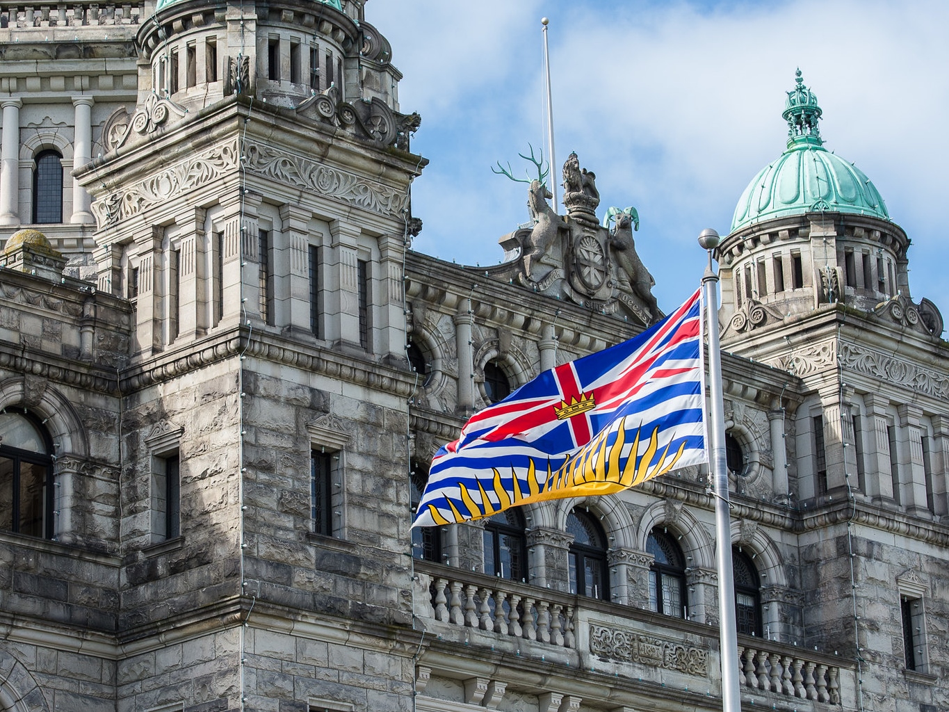 A B.C. flag flies in front of the stone legislature building.