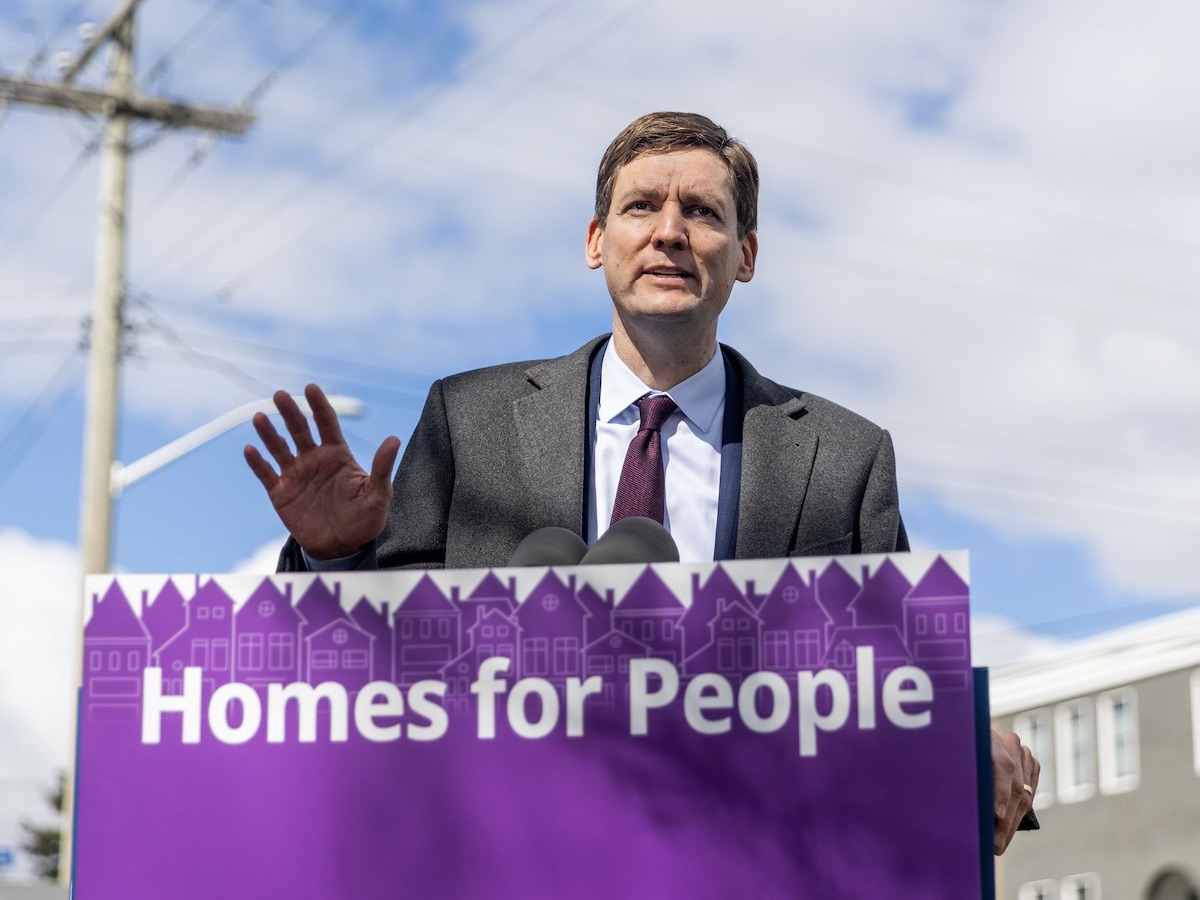Premier David Eby stands behind a podium with a sign saying “Homes for People.”
