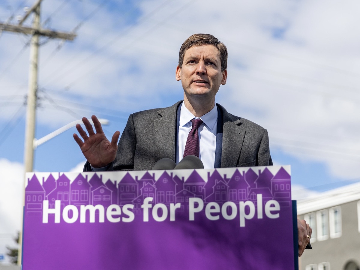 Premier David Eby stands behind a podium with a sign saying &ldquo;Homes for People.&rdquo;