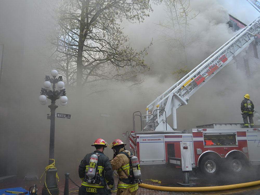 Firefighters and a ladder truck face a smoke-filled scene.