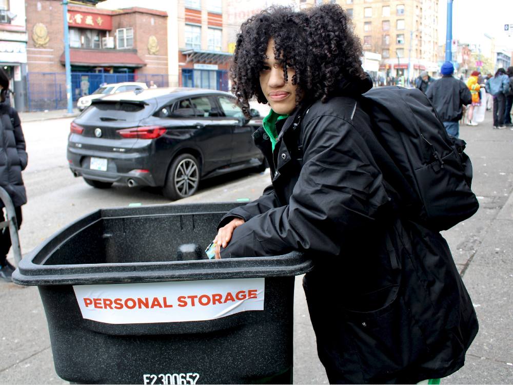 A person wearing black leans on a garbage bin labelled &ldquo;PERSONAL STORAGE&rdquo; on East Hastings Street.