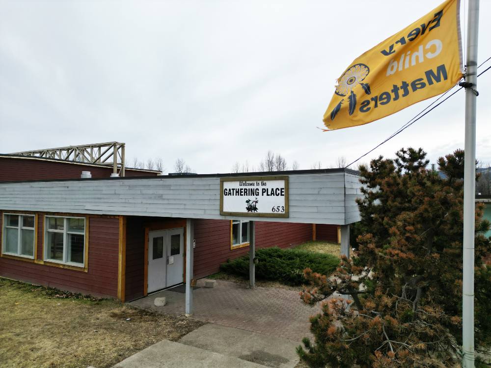 A building with a sign over the door that says "welcome to the gathering place." To the right of the building is an orange flag that says "every child matters."