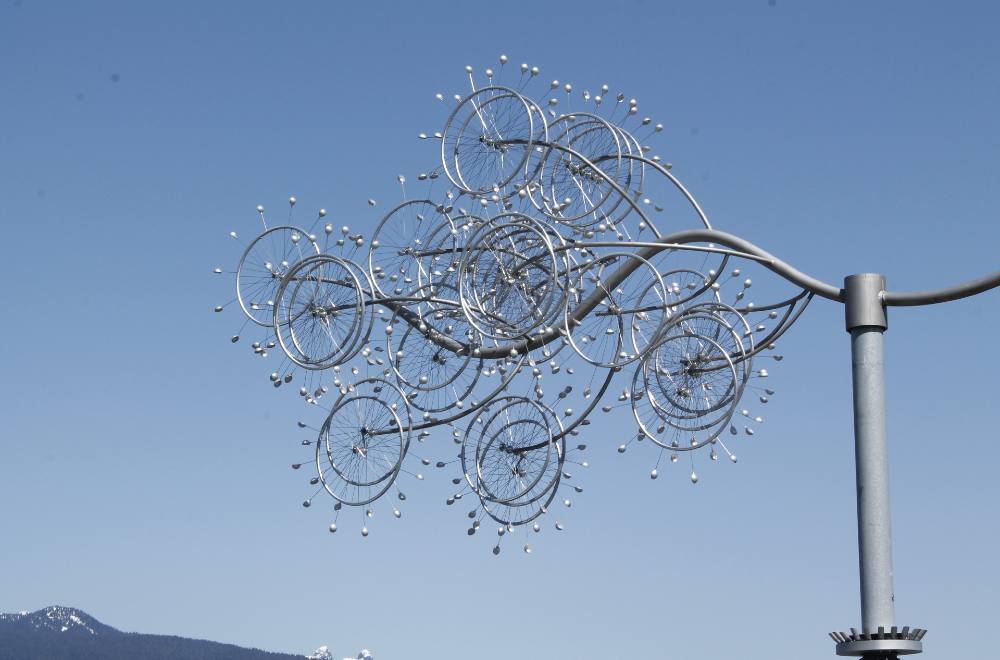 A silver sculpture composed of a large number of wheels appears in a blue sky.