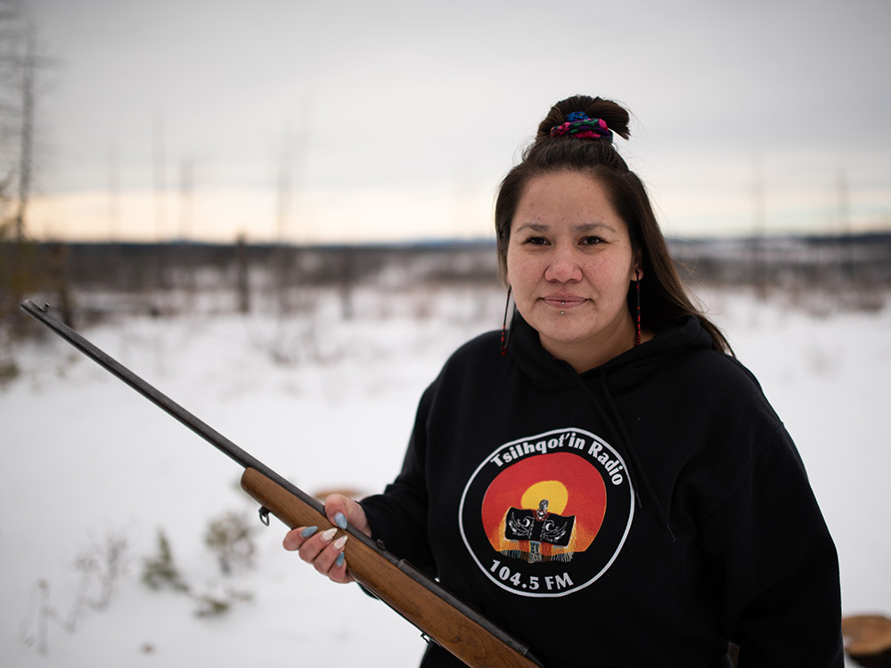 A woman standing in a snowy field with a rifle.