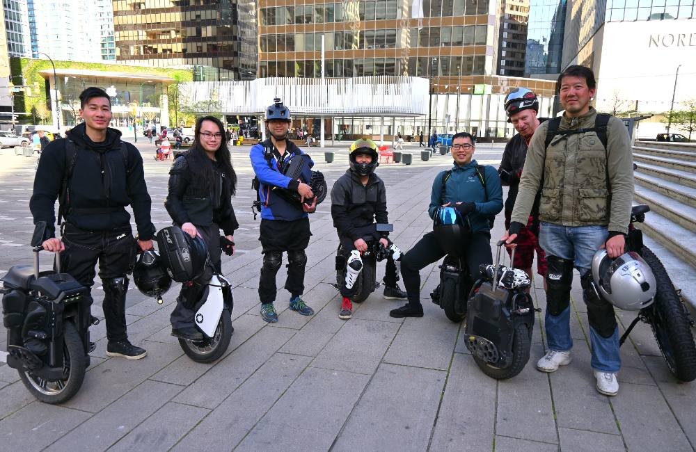 Seven people with protective gear and electric unicyles stand and smile outside of the Vancouver Art Gallery.