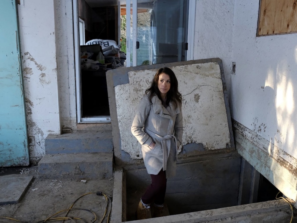 A woman with long brown hair stands amidst a water damaged home.
