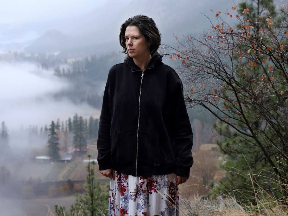 A woman stands on a mountain with fog rolling in behind her.