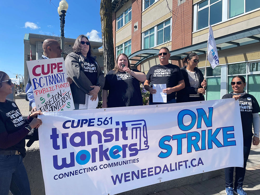 A group of workers wearing black T-shirts hold a white banner that says &lsquo;On strike.&rsquo;