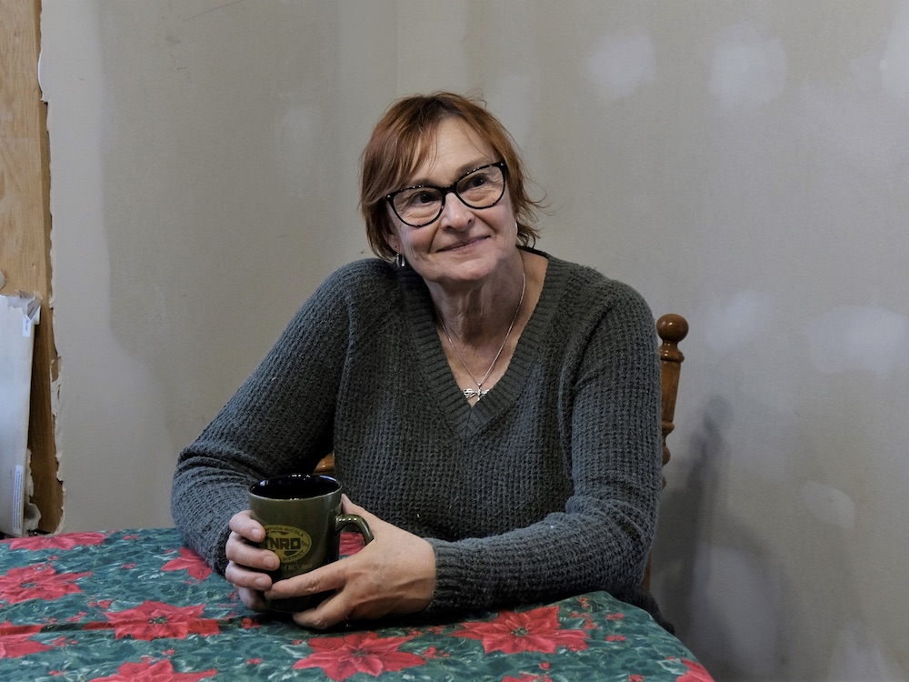 A woman in a green sweater sits at a table holding a mug.