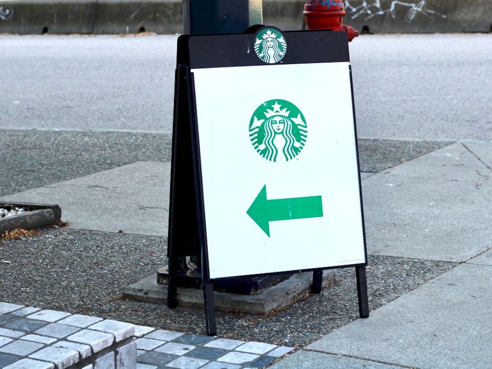 A sidewalk sandwich board sign with a Starbucks logo and an arrow pointing off camera.