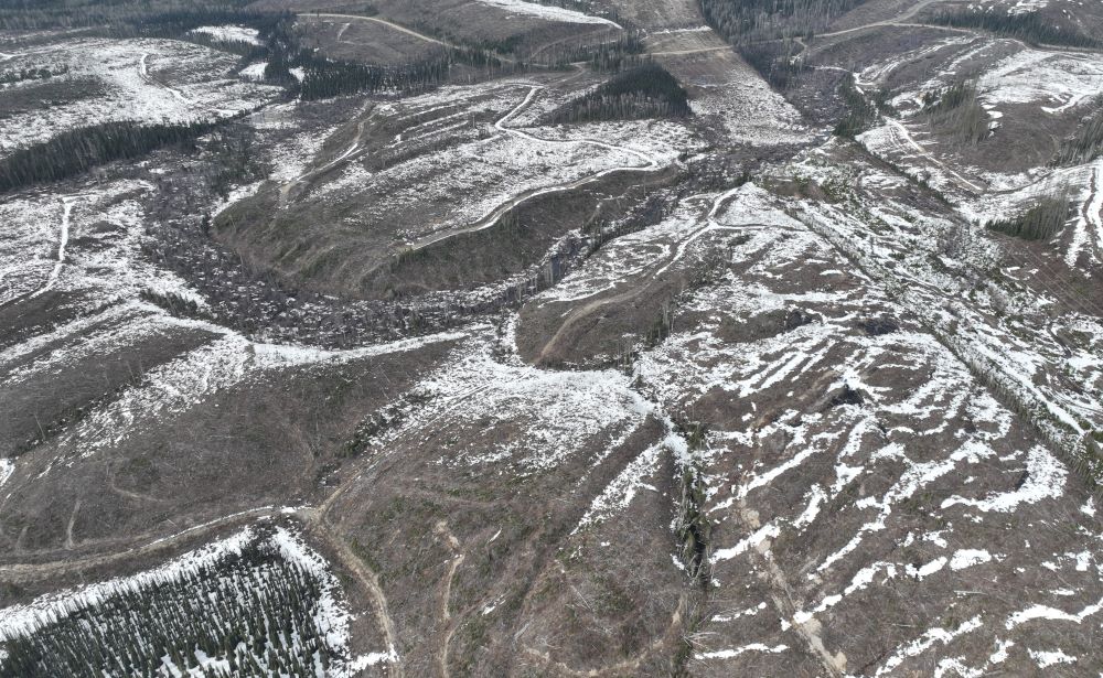 From the air, a snowy landscape of rolling mountaintops barren of trees stretches far.