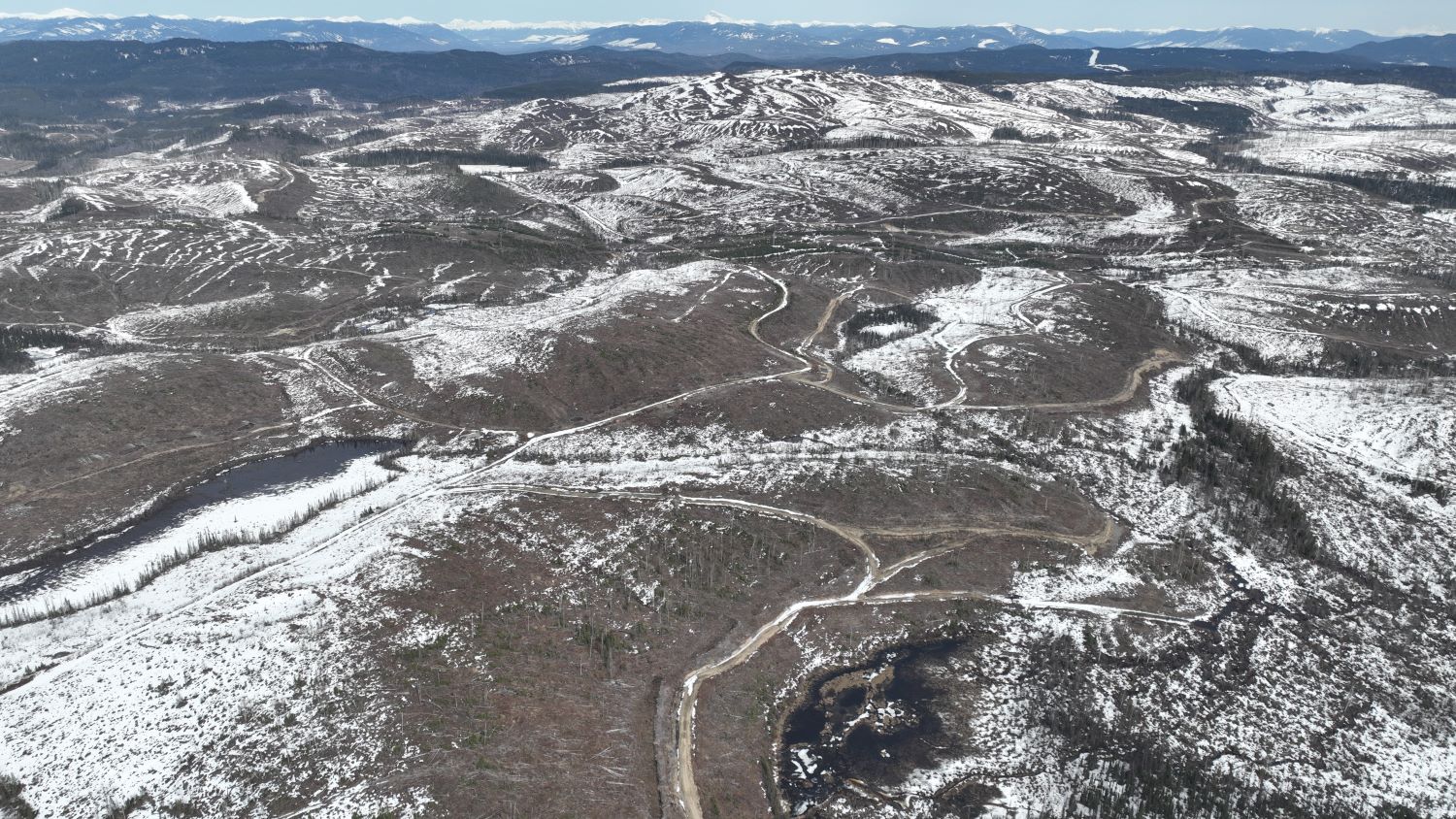 From the air, a snowy landscape of rolling mountaintops barren of trees stretches far.